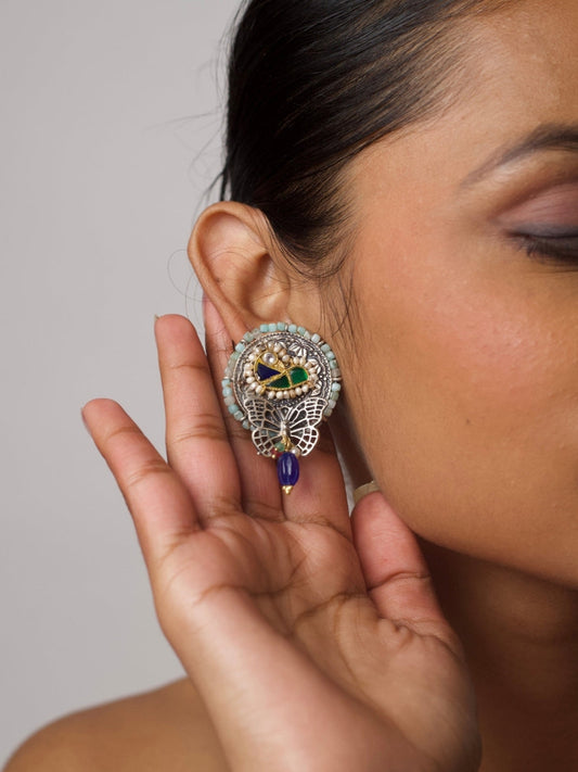 Close-up of Naksa's Titliyaan Silver Drops featuring 92.5 silver butterfly design, pearl inlay, enamel work, and dangling indigo bead on a woman's ear.