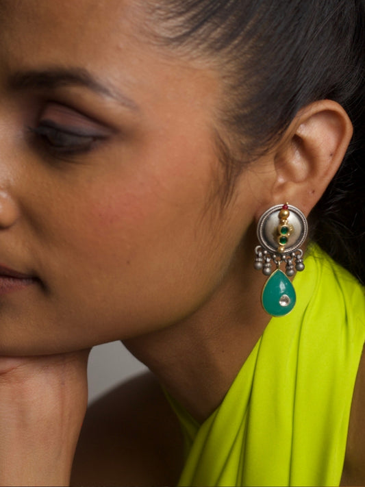 Close-up of handcrafted fusion earrings in 92.5 silver with turquoise drop, coin motif top, and dangling silver beads, worn with lime green fabric