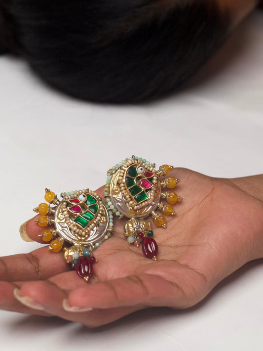 Close-up of Mor-mukut Studs in pure silver with gold polish, featuring enamelled parrot design, tiny elephant motif, crown-like side extensions, gemstone beadwork, and pearl borders.