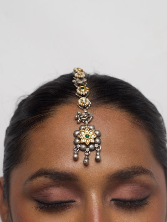 Close-up of The Gardenia Maang Tikka in pure 92.5 silver with kundan setting, green center stone, and dangling beads worn on forehead.