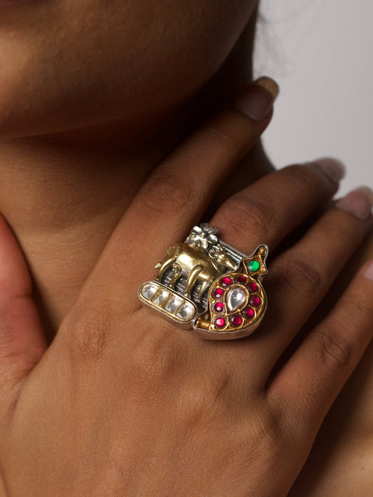 Close-up of a handcrafted 92.5 silver fusion ring with a golden cow, crescent paisley motif, and red-green gemstone detailing, inspired by Pichwai art.