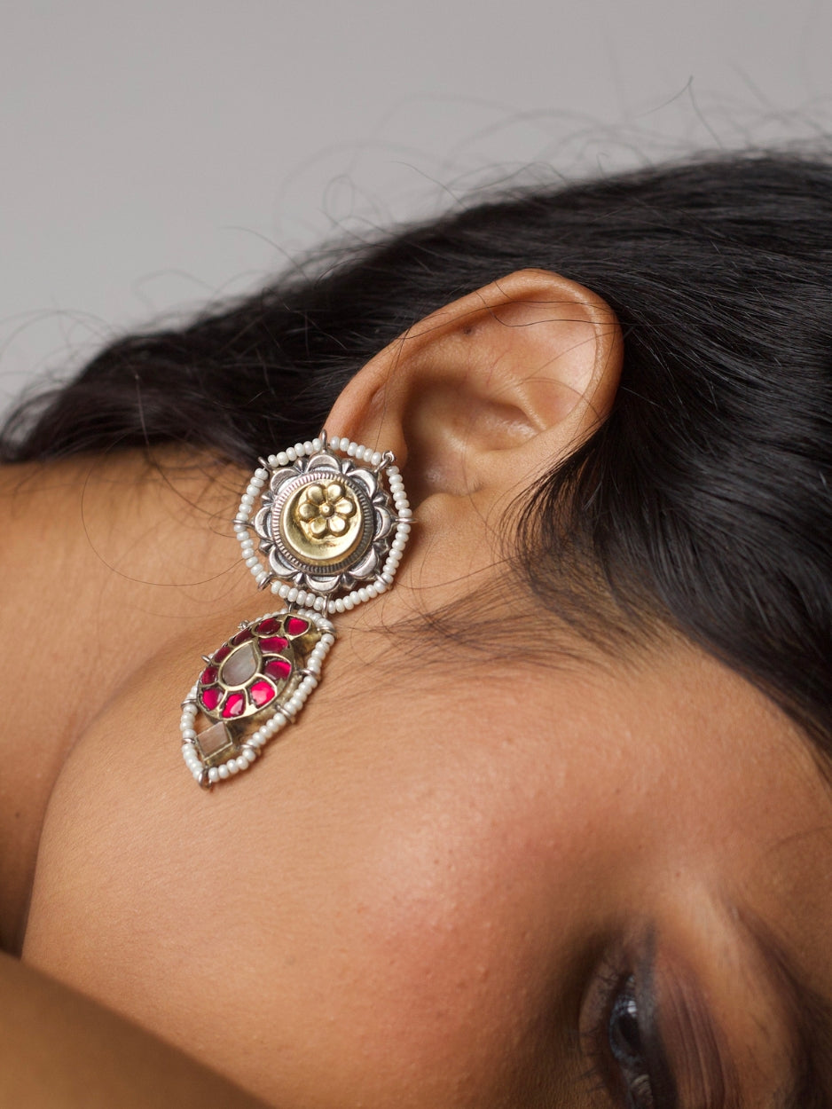 Close-up of The Petal Pact Earrings featuring a 92.5 silver base, golden floral motif with pearls on top, and a bold pink-stone drop element—styled on ear.